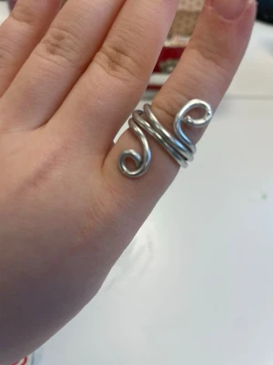 Silverfärgad ring - Säljer en silverfärgad ring böjd i unik form. Ringen består av silverfärgad metalltråd böjd i en spiral, och i ändarna på tråden så är den böjd i två små cirklar. Perfekt för dig som vill ha ett kreativt smycke. 