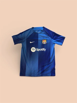 Blå FC Barcelona matchtröja Nike - Snygg blå FC Barcelona matchtröja från Nike med klubbmärke och Spotify-logga på bröstet. Tröjan har korta ärmar och ett mönster i olika blå nyanser. Perfekt för dig som älskar fotboll och vill visa ditt stöd för Barca.