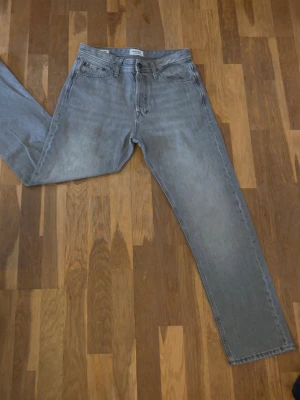 Grå raka jeans från Jack & Jones - Snygga grå jeans från Jack & Jones med rak passform och klassisk femficksdesign. Jeansen har en diskret tvättad look och är tillverkade i slitstarkt denimtyg. Perfekta för en avslappnad och trendig stil.