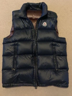 Moncler väst - Jag säljer denna blåa moncler västen utan luva. Storlek 2 den passar mig som är 178 och väger 65 kg.