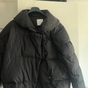 Svart pufferjacka från Mango - Säljer en svart pufferjacka från Mango med oversized krage och tryckknappar framtill. Jackan har en boxig passform och är perfekt för kalla dagar. Materialet är syntet och jackan är helsvart utan mönster. Snygg och enkel att styla till vintern.