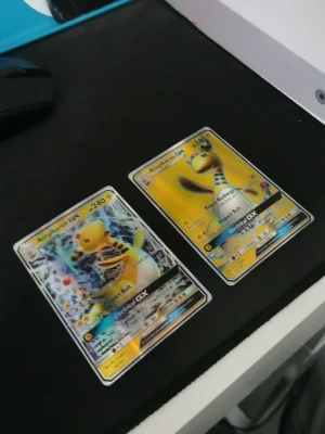 Två Ampharos GX Pokémonkort - Säljer två Ampharos GX samlarkort från Pokémon TCG. Båda korten har färgstarka illustrationer med gul och svart design, holografiska detaljer och tydliga Pokémon-loggor på baksidan. Perfekt för dig som vill utöka din samling eller spela TCG.