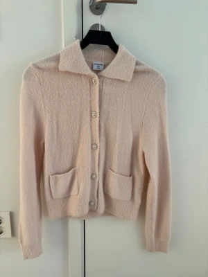 Ljusrosa kofta med fickor - Supersöt ljusrosa kofta med klassisk krage, knäppning framtill och två stora fickor. Mjuk och fluffig känsla, perfekt för lager på lager. Långärmad och med ribbade muddar vid ärmslut och nederkant.