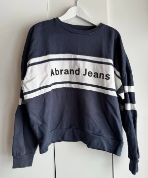 Mörkblå sweatshirt från Abrand Jeans - Cool mörkblå sweatshirt från Abrand Jeans med vita ränder och logga framtill. Storlek S. Tröjan har rund hals, långa ärmar, breda muddar och nedhasade axlar. Mjuk o superskön kvalitét. Perfekt för en avslappnad och trendig look.  Använd 1 gång. Skrynklig på bilderna men den är i jättefint skick. 