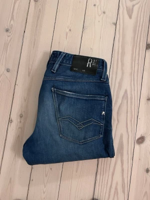 Blå jeans från Replay herr - Säljer ett par schysstare anbass jeans ifrån replay. Cool detalj på bakfickorna där det inte är en söm, då tyget är tryckt med samma mönster som skapar en cool design. Riktigt bra skick på brallorna. Hör av dig vid minsta fundering