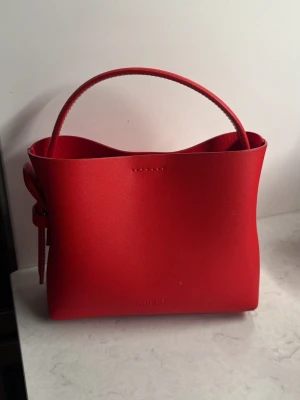 Röd handväska mini -  Arket - Snygg röd handväska från Arket i äkta läder. Väskan har både handtag samt längre band för att kunna bäras cross body.  Så gott som ny, endast använd vid ett fåtal tillfällen.
