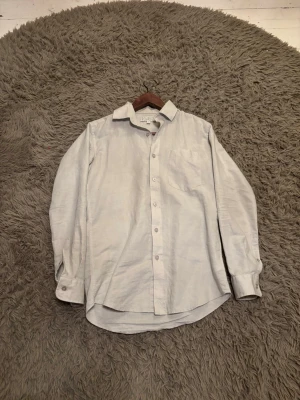 Ljusbeige linneskjorta från Ahlquist Clothing - Säljer en stilren ljusbeige skjorta från Ahlquist Clothing i storlek XS. Skjortan är tillverkad i linne, har klassisk krage, bröstficka och knappar framtill. Broderad logga vid nederkanten ger en clean detalj. Perfekt för dig som gillar minimalistisk stil. Använd endast en gång och är som ny. Vill du ha fler bilder är det bara att skicka dm🤗