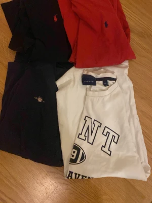 T-shirtpaket från GANT & Ralph Lauren - Säljer ett paket med fyra t-shirts från GANT och Ralph Lauren. Färgerna är svart, röd, marinblå och vit. T-shirtsen har klassiska loggor på bröstet och är i bomull. Perfekta basplagg med normal passform och korta ärmar.