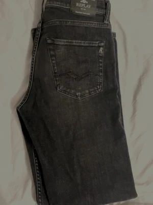 Svarta Replay jeans med raka ben - Snygga svarta jeans från Replay med klassisk femficksmodell och raka ben. Jeansen har diskreta slitningar och en mörk tvätt som ger en cool look. Märkeslapp bak i midjan och detaljerade sömmar på bakfickan.