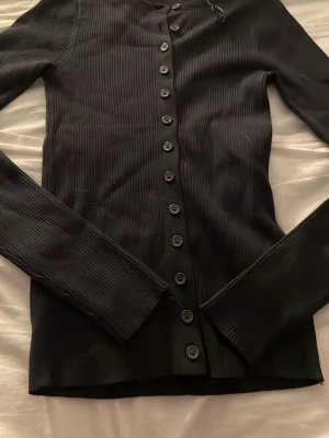 Blå ribbad kofta med knappar - Snygg blå ribbad kofta med långa ärmar och knäppning hela vägen framtill. Koftan har en smal passform och är tillverkad i ett stretchigt material som sitter skönt på kroppen. Perfekt att styla lager på lager eller bära som den är.