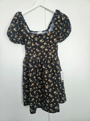 Blommig kortklänning från Miss Selfridge - Supersöt svart kortklänning från Miss Selfridge med små gula blommor och puffärmar. Klänningen har en markerad midja och en lätt utställd kjol. Perfekt för dig som gillar romantiska detaljer och blommigt mönster.
