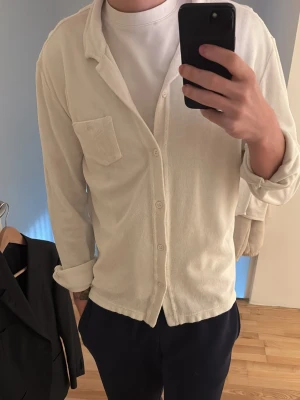 Vit frottéskjorta med ficka - Säljer en vit skjorta i mjuk frotté med klassisk krage och knappstängning framtill. Skjortan är i size medium men funkar även perfekt för large, den e aldrig använd och köptes för 1500kr så här får ni en kanondeal.