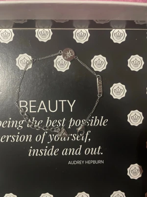 Silverfärgat armband från Guess - Snyggt silverfärgat armband från Guess med tunn kedja och små berlocker, inklusive en rund bricka med stjärndesign och en rektangulär bricka med Guess-loggan. Perfekt accessoar för att lyfta din stil.