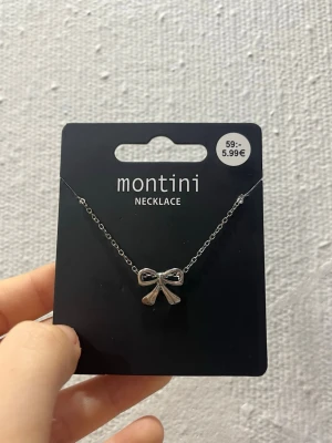 Silverfärgat halsband från ur&penn  - Snyggt halsband från ur&penn i silverfärg med en söt rosett som hänge. Kedjan är tunn och elegant, och rosetten ger en gullig och trendig touch till din outfit. Perfekt accessoar för dig som gillar stilrena smycken med en twist.