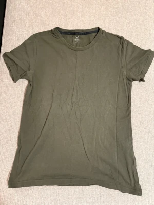 Olivgrön t-shirt från SOC - En enkel och stilren olivgrön t-shirt från SOC. T-shirten har rund halsringning och korta ärmar. Tillverkad i mjuk bomull som känns skön mot huden. Perfekt basplagg att matcha med jeans eller shorts.