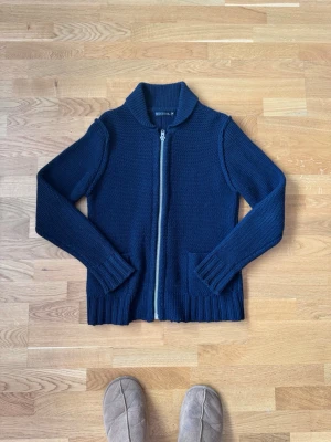 Mörkblå stickad cardigan från filippa K - Mörkblå stickad tröja med dragkedja framtill och två fickor. Tröjan har ribbade muddar vid ärmslut och nederkant samt en hög krage. Perfekt för lager på lager och enkel att matcha med olika outfits. (wool blend, cirka 80% ull 20% bomull 