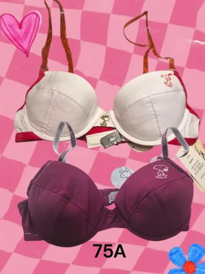 Två Snoopy BH:ar storlek 75A - Säljer två helt oanvända Snoopy-behåar från början av 2000-talet. Den vita har röda detaljer, halvgenomskinliga orangea axelband som är avtagbara, en liten silverberlock mellan kuporna och Snooben-tryck på ena kupan. Den vinröda har axelband med texttryck och Snobbentryck i vitt på ena kupan. Bägge har tunna urtagbara inlägg. Kommer från ett restlager och har lapparna kvar. Se även mina andra anonnser, du får 20% bundlerabatt om du köper flera. 