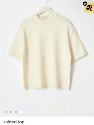 Krämvit stickad topp från Arket - Minimalistisk krämvit stickad topp från gina med korta ärmar och rund halsringning. Tillverkad i mjukt material med ribbade kanter. Perfekt för en clean och stilren look. Prislappen kvar