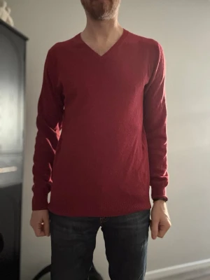 Röd V-ringad tröja - Snygg röd tröja med V-ringning och långa ärmar. Tröjan har en enkel och stilren design med ribbade muddar vid ärmslut och nederkant. Perfekt att matcha med jeans för en clean look.