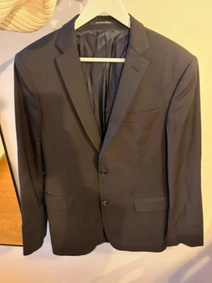 Oscar Jacobson kavaj - Stilren svart kavaj från Oscar Jacobson med två knappar framtill, klassisk passform och diskreta fickor. Perfekt för dig som vill ha en enkel och snygg look. Enkel slits bak och helfodrad insida. Kavajen har inga defekter och är dessutom Cotton stretch som gör den mjuk och väldigt skön när du har på den. Storleken är 148 vilket är som 48 fast en längre modell. 