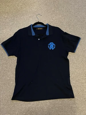 Mörkblå piké från Roberto Cavalli - Snygg mörkblå pikétröja från Roberto Cavalli med blå logga broderad på bröstet. Denna är i storlek L men passar även M