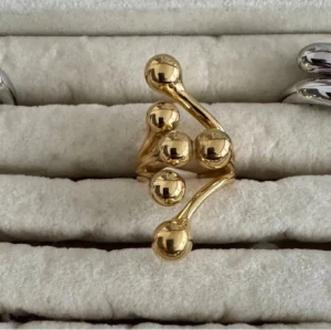 Guldfärgad statementring med kulor - Unik guldfärgad ring med fem blanka kulor i modern, asymmetrisk design. Ringen har en skulptural form som verkligen sticker ut och ger en trendig look. Perfekt för dig som gillar accessoarer som syns och vill ha något annorlunda.
