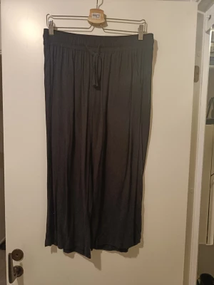 Svarta vida tunna byxor, perfekt för sommaren - Säljer ett par svarta tunna byxor med bred resår i midjan och justerbar dragsko. Byxorna har en lös och avslappnad passform med raka, vida ben. Tillverkade i ett mjukt och stretchigt material som känns skönt mot huden. Perfekta för chill dagar eller när du vill vara bekväm.oclså perfekt till sommaren. Använda enstaka gång. 