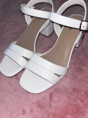 Vita sandaler med blockklack - Stilrena vita sandaler från skopunkten med breda remmar och fyrkantig tå. Sandalerna har en justerbar ankelrem med silverfärgat spänne och en stabil blockklack. Tillverkade i syntetmaterial med en mjuk innersula för extra komfort. Använda endast 1 gång. Köpta för 400kr ( prislapp kvar se bild 5 sista bilden ) 