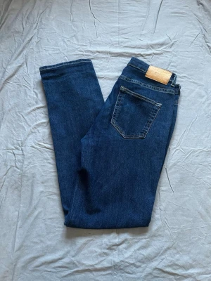 Mörkblå jeans från SH EASE - Snygga mörkblå jeans från SH EASE med klassisk femficksdesign och raka ben. Jeansen har en läderpatch med logga bak i midjan och är tillverkade i ett mjukt denimtyg som känns bekvämt hela dagen.