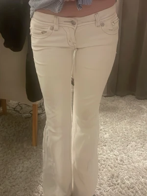 Vita Miss Me jeans med diamanter - Säljer ett par vita jeans från Miss Me med snygga strassdetaljer och broderier på bakfickorna. Jeansen har raka ben och dekorativa knappar på fickorna. Perfekta för dig som vill sticka ut med lite extra bling. Dom är low waist men bootcut som är tillsytt
