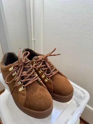 Bruna Gant sneakers med mocka och snörning - Säljer ett par bruna sneakers i mocka med guldfärgade metalldetaljer och bruna snören med vita prickar. Insidan är fodrad med mjukt material för extra komfort. Snygg och chunky sula som ger en modern look.