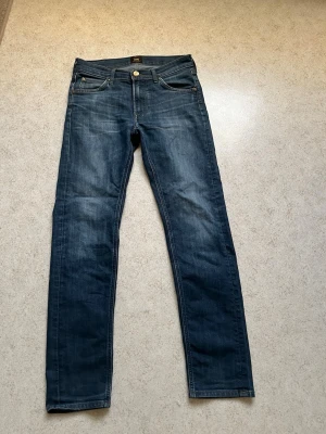 Mörkblå jeans från Lee - Snygga mörkblå jeans från Lee med klassisk femficksdesign och raka ben. Jeansen har subtila slitningar och en läderpatch med logga bak i midjan. Tillverkade i denim med en autentisk tvättad look. Storlek W29 L32. Öppen för förhandling