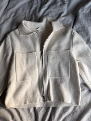 Vit ziptröja från Åhléns  - Säljer en stilren vit ziptröja från Å Woman i storlek XS. Tröjan har två stora fickor framtill, dragkedja och en mjuk, stickad känsla. Perfekt till lager på lager och enkel att matcha med olika outfits.