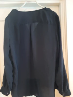 Svart blus från Divided H&M - Stilren svart blus från Divided H&M med två bröstfickor och knappar framtill. Blusen har en lös passform och är tillverkad i ett tunt, lätt material som ger en snygg flowy look. Perfekt att matcha med jeans eller kjol.