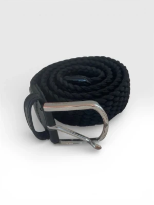 Svart flätat bälte från John Henric - Snyggt svart flätat bälte från John Henric med silverfärgat spänne. Bältet har en klassisk design och är gjort i ett mjukt syntetmaterial med detaljer i skinn. Perfekt för att lyfta vilken outfit som helst.