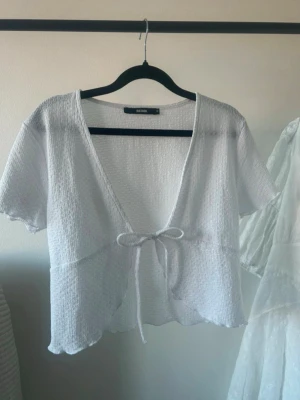 Vit croppad topp med knyt från BikBok - Säljer en vit croppad topp från BikBok med korta ärmar och v-ringning. Toppen har en snygg knytning framtill och är gjord i ett lätt, strukturerat tyg som känns luftigt. Perfekt till sommaren och enkel att styla med jeans, kjol eller över bikini. Säljer då den tyvärr inte kommer till användning, helt oanvänd. Det är bara skriva vid frågor! 🩷Kolla gärna mina andra plagg, går att köpa med bundelrabatt! 