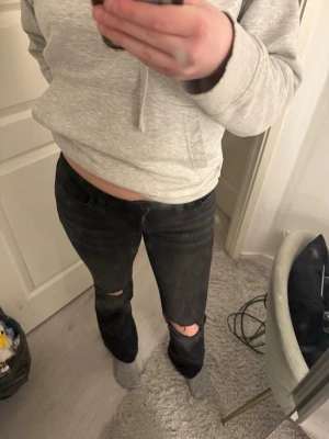 Nelly jeans  - Säljer ett par svarta jeans med hål på båda knäna och lätt utsvängda ben. Jeansen har en klassisk femficksmodell och normal midja. Perfekta för dig som gillar en avslappnad och trendig stil.