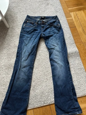 Blå bootcut jeans från LTB - Säljer ett par blå bootcut jeans från LTB med klassisk femficksdesign och snygga slitningar framtill. Jeansen har kontrastsömmar och en bekväm midja. Perfekta för dig som gillar en avslappnad men ändå trendig look.
