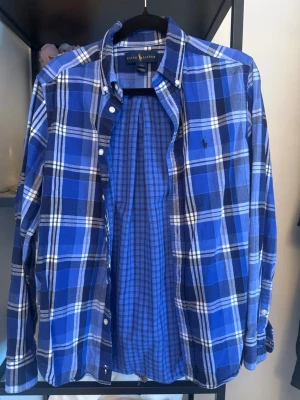 Blårutig skjorta från Ralph Lauren - Snygg blårutig skjorta från Ralph Lauren med klassisk button-down krage och broderad logga på bröstet. Stolen Dm
