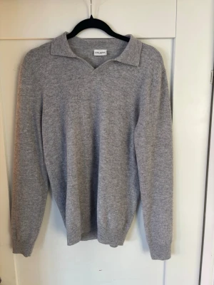 Grå stickad tröja från John Henric - Klassisk grå stickad tröja från John Henric med krage och v-ringning. Tröjan har långa ärmar och ribbade muddar vid ärmslut och nederkant. Perfekt för lager på lager och enkel att matcha med olika outfits.