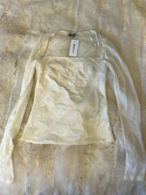Ljus blus/ topp från Gina Tricot - Säljer en ljus blus från Gina Tricot med subtilt blommönster i tyget. Blusen har långa ärmar och en rak, något figurnära passform. Helt ny med prislapp kvar!