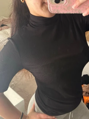 Svart ribbad polotopp - Säljer en svart ribbad polotopp med halvlång ärm. Toppen har en tight passform och är tillverkad i ett mjukt stretchigt material som sitter snyggt på kroppen. Perfekt att styla med både jeans och kjol för en clean look.