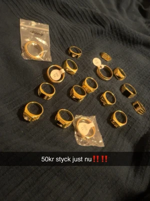 Guldiga ringar med olika former - Säljer flera guldiga ringar i olika former och storlekar. Vissa ringar har stenar eller detaljerade mönster, medan andra är mer enkla och släta. Perfekta för att mixa och matcha till din egen stil. Alla ringar är i metall och har en trendig look. Styck pris.