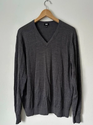 Mörkgrå V-ringad tröja Uniqlo - Stilren mörkgrå stickad tröja från Uniqlo med V-ringning och långa ärmar. Tillverkad i tunt, mjukt material som passar perfekt för lager på lager. Klassisk passform och ribbade muddar vid ärmslut och nederkant. 8A15