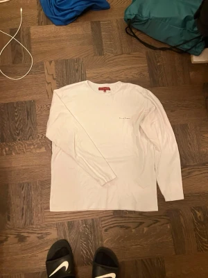 Vit långärmad topp från Philip Russel - Säljer en stilren vit långärmad topp från Philip Russel. Toppen har en enkel design med diskret logga på bröstet och rund halsringning. Perfekt att matcha med jeans eller kjol för en clean look.