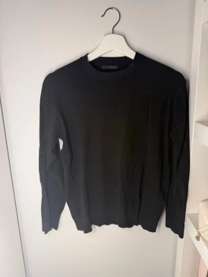 Svart stickad tröja i basic stil - En enkel och stilren svart stickad tröja med rund halsringning och långa ärmar. Tröjan har en klassisk passform och ribbade muddar vid ärmslut och nederkant. Perfekt att matcha med jeans eller kjol för en clean look.