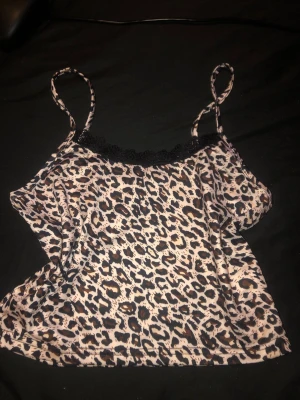 Leopardmönstrad linnetopp med spets - Säljer en leopardmönstrad linnetopp med tunna axelband och svart spetsdetalj längs urringningen. Toppen har en ljus bas med bruna och svarta leopardfläckar. Perfekt för dig som vill sticka ut lite extra.