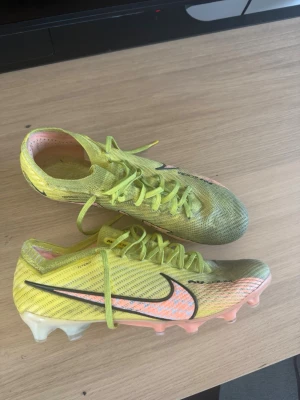 Nike Mercurial Vapor gul fotbollssko - Säljer ett par Nike Mercurial Vapor fotbollsskor i gul färg med svarta och rosa detaljer. Skorna har en låg profil, snörning och syntetiskt material för lätt vikt och bra bollkontroll. Sulan har dobbar i plast för spel på gräs. Perfekt för dig som vill ha speed på planen.