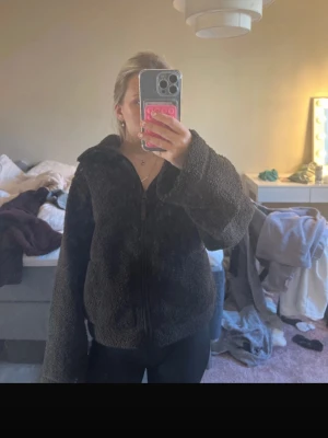 Brun teddyjacka med dragkedja - Mysig brun teddyjacka med dragkedja framtill och breda ärmar. Jackan har en fluffig och mjuk struktur i teddy-material som håller dig varm. Perfekt för att slänga på sig när det är kyligt ute.