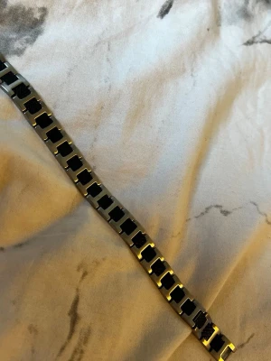 Lacoste armband i stål och svart mesh - Snyggt armband från Lacoste i rostfritt stål med svarta meshdetaljer. Länkarna har en modern, fyrkantig form och armbandet har en diskret Lacoste-logga på spännet. Perfekt accessoar för dig som gillar stilrena och sportiga smycken.